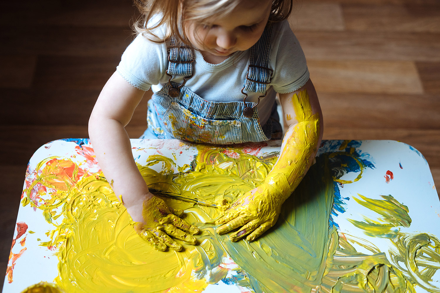 Little girl painting with a lot of colors using her hands